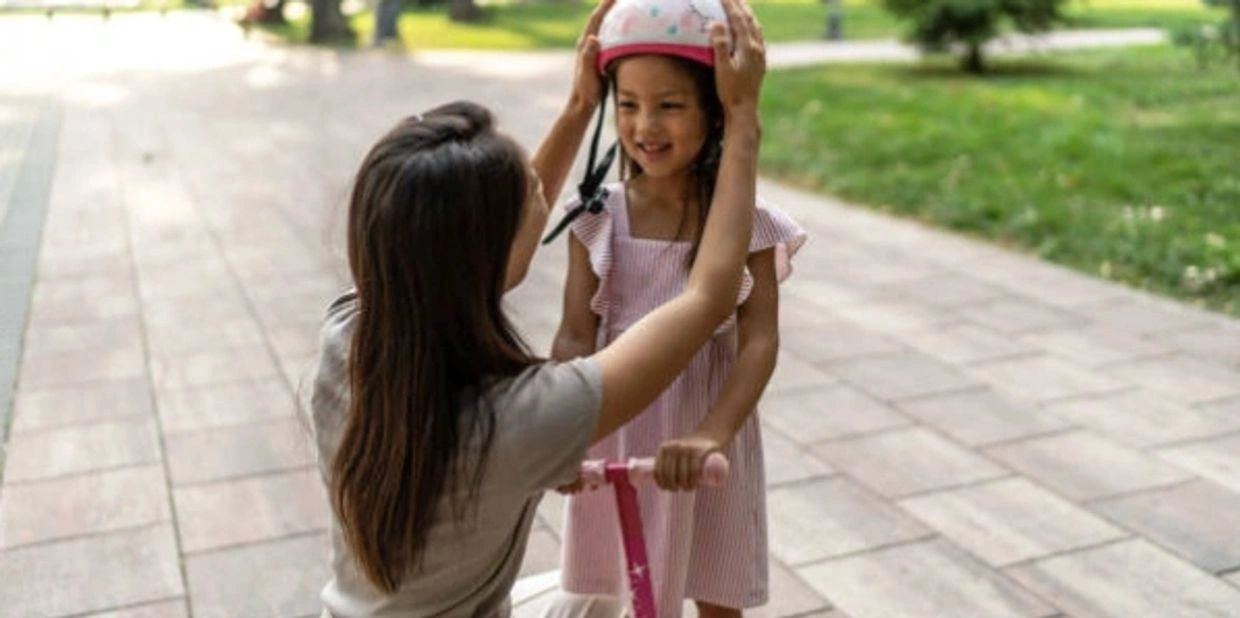A woman helping a child put on her helmet.